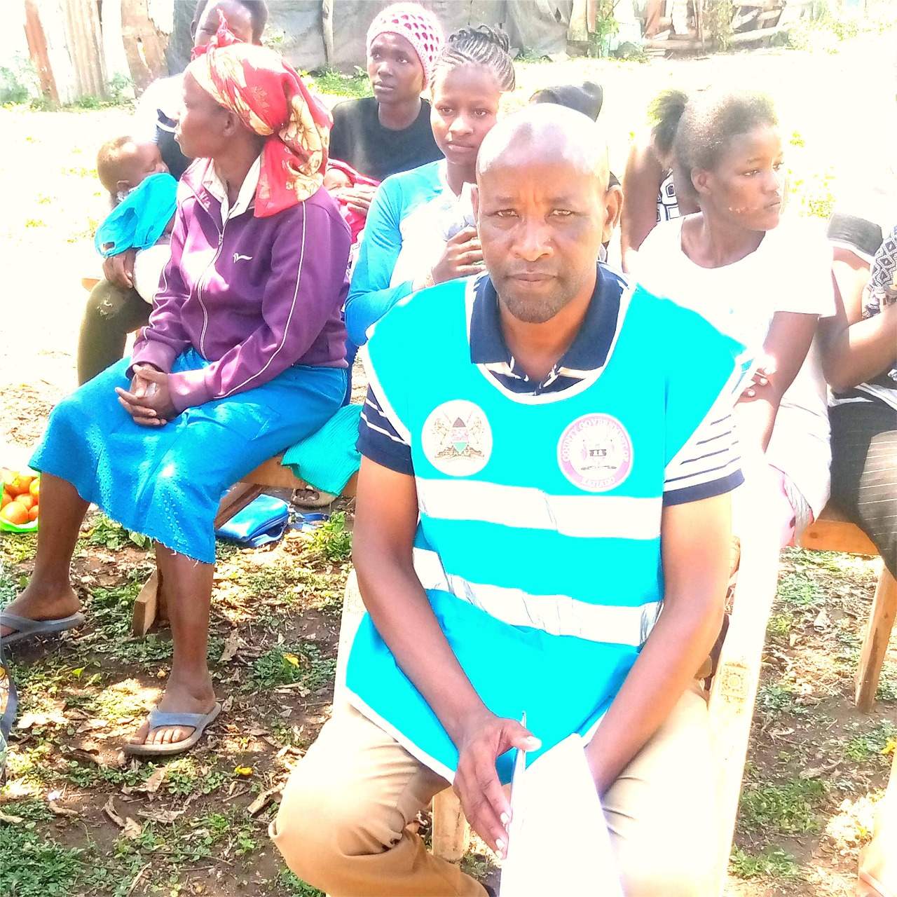 A community health promoter in a volunteer vest speaking with residents