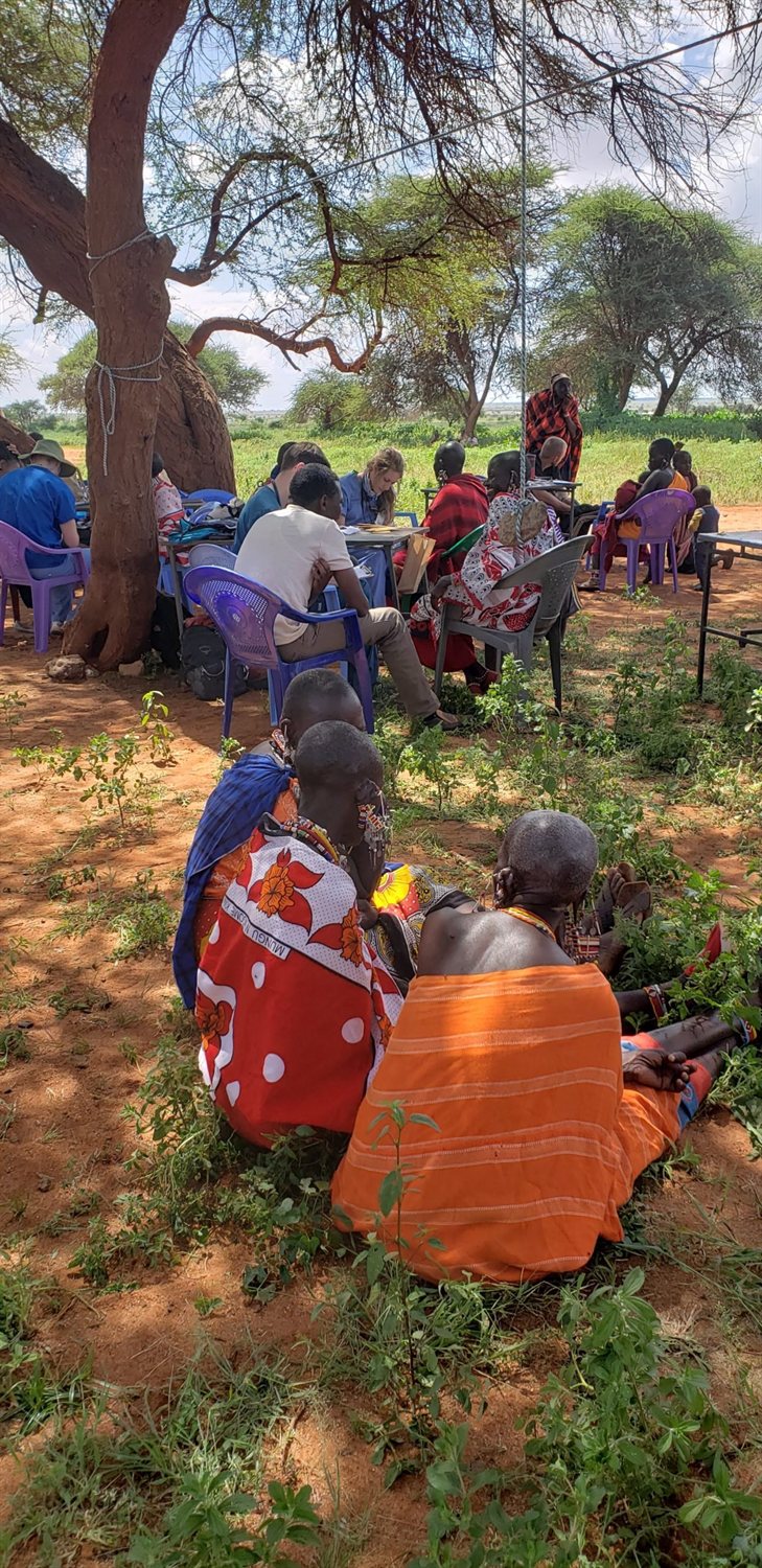 A community gathering under an acacia tree during an outreach